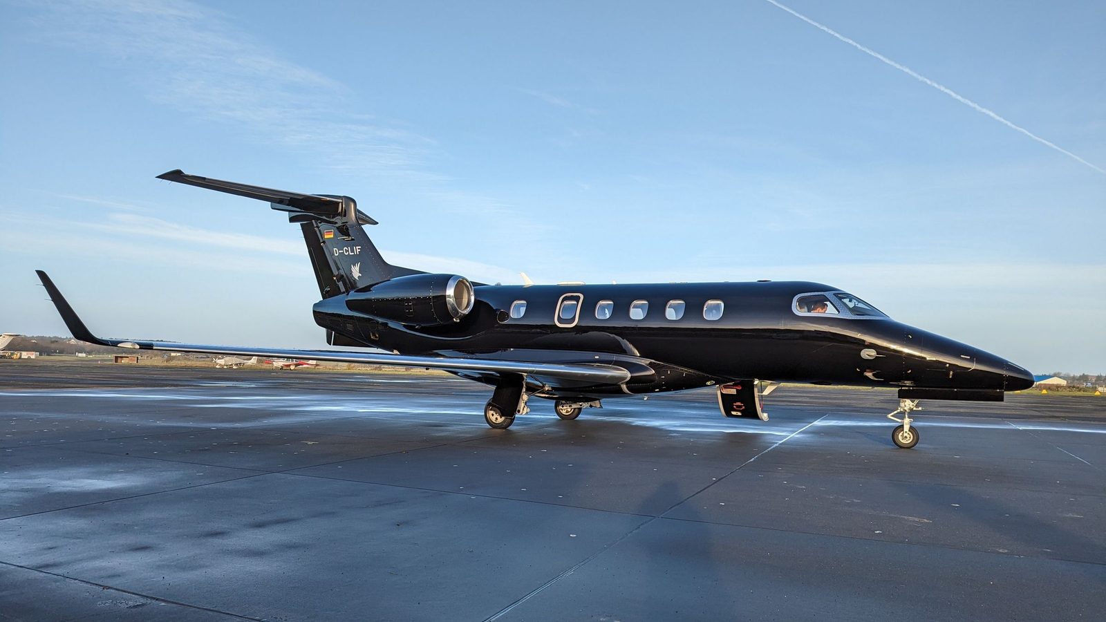 A white private jet parked on a sunny tarmac under a blue sky